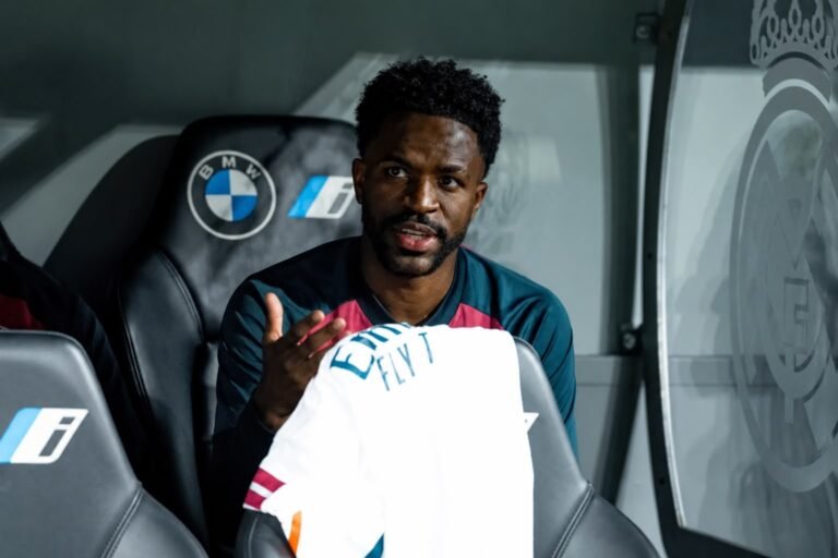 Real Madrid player seated on the substitutes’ bench holding a white shirt.