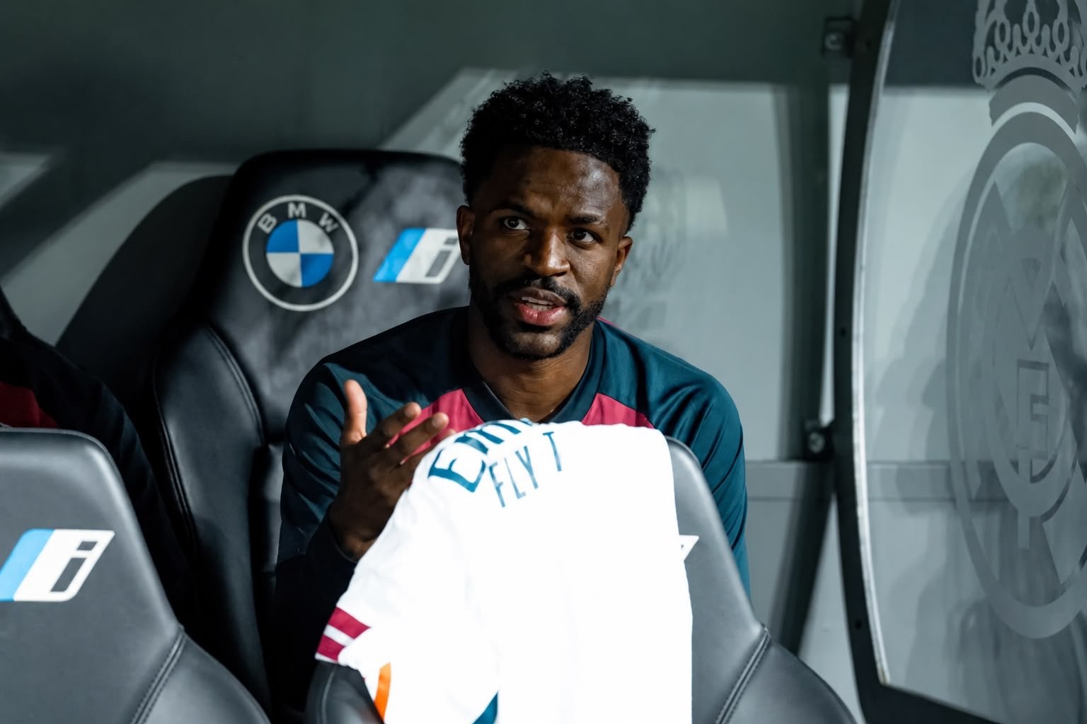 Real Madrid player seated on the substitutes’ bench holding a white shirt.
